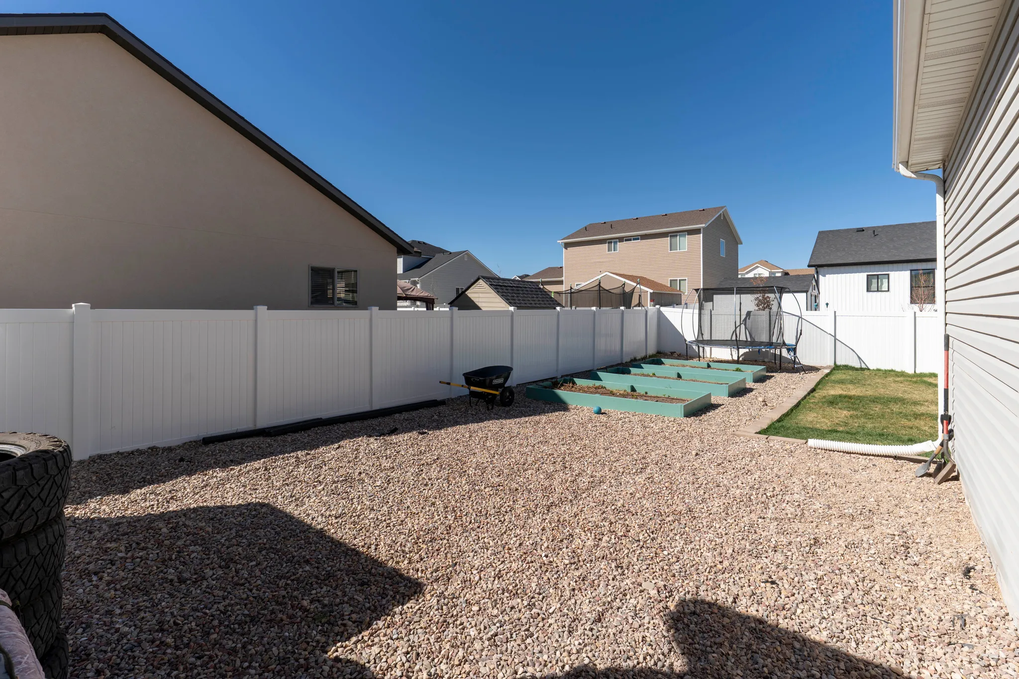 Fenced backyard featuring a trampoline, a patio, a residential view, and a garden