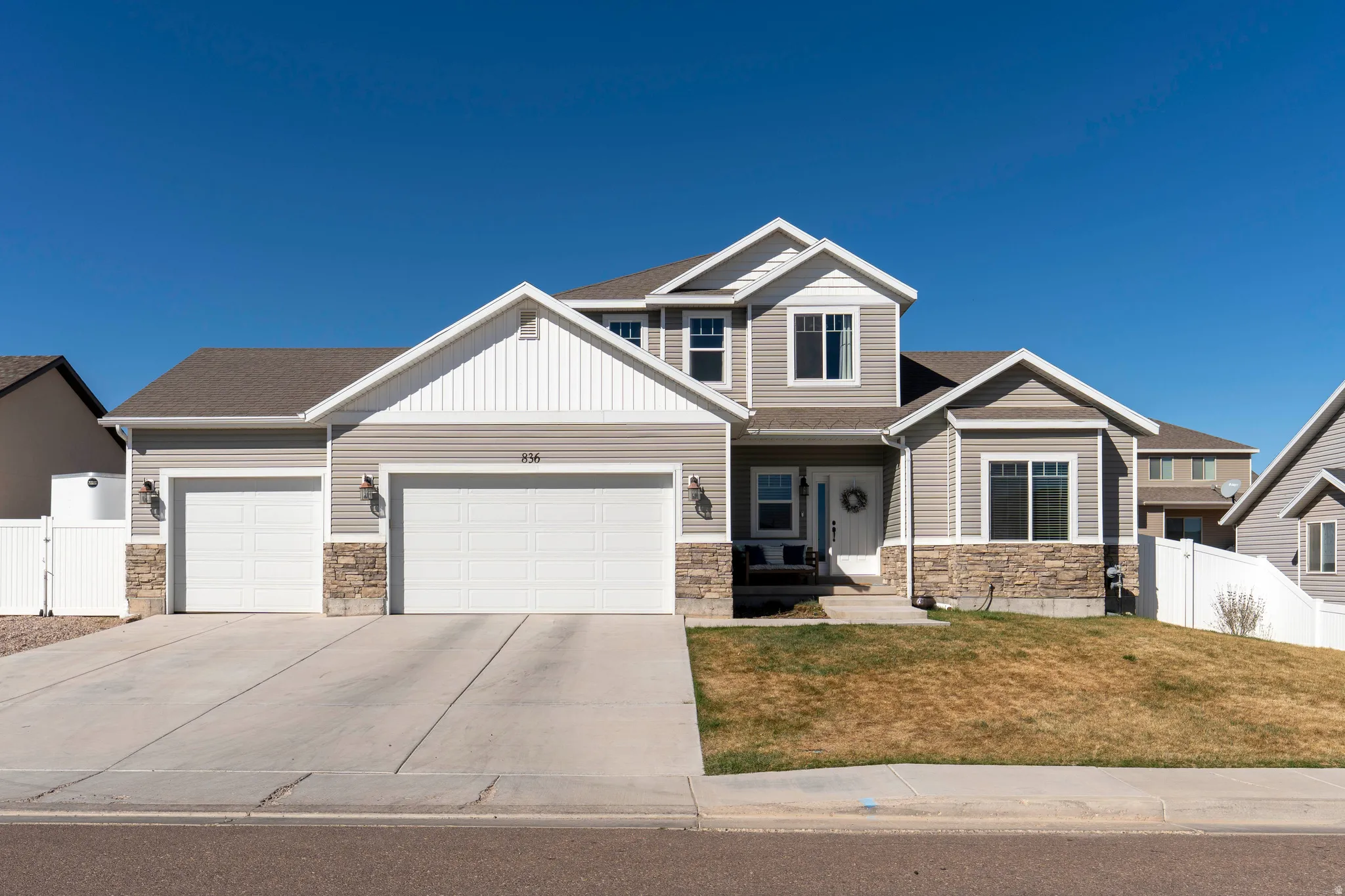 Craftsman-style house with stone siding, an attached garage, driveway, and a gate