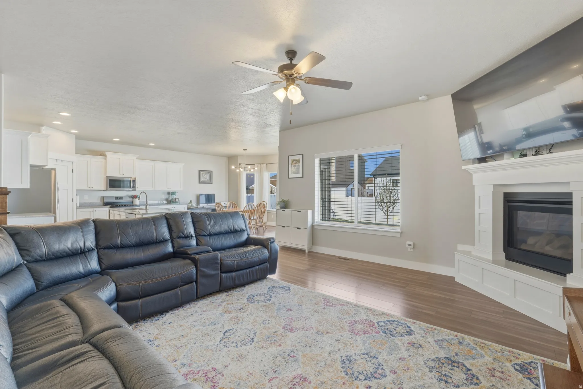 Living room featuring a ceiling fan, dark wood-type flooring, a glass covered fireplace, and a chandelier