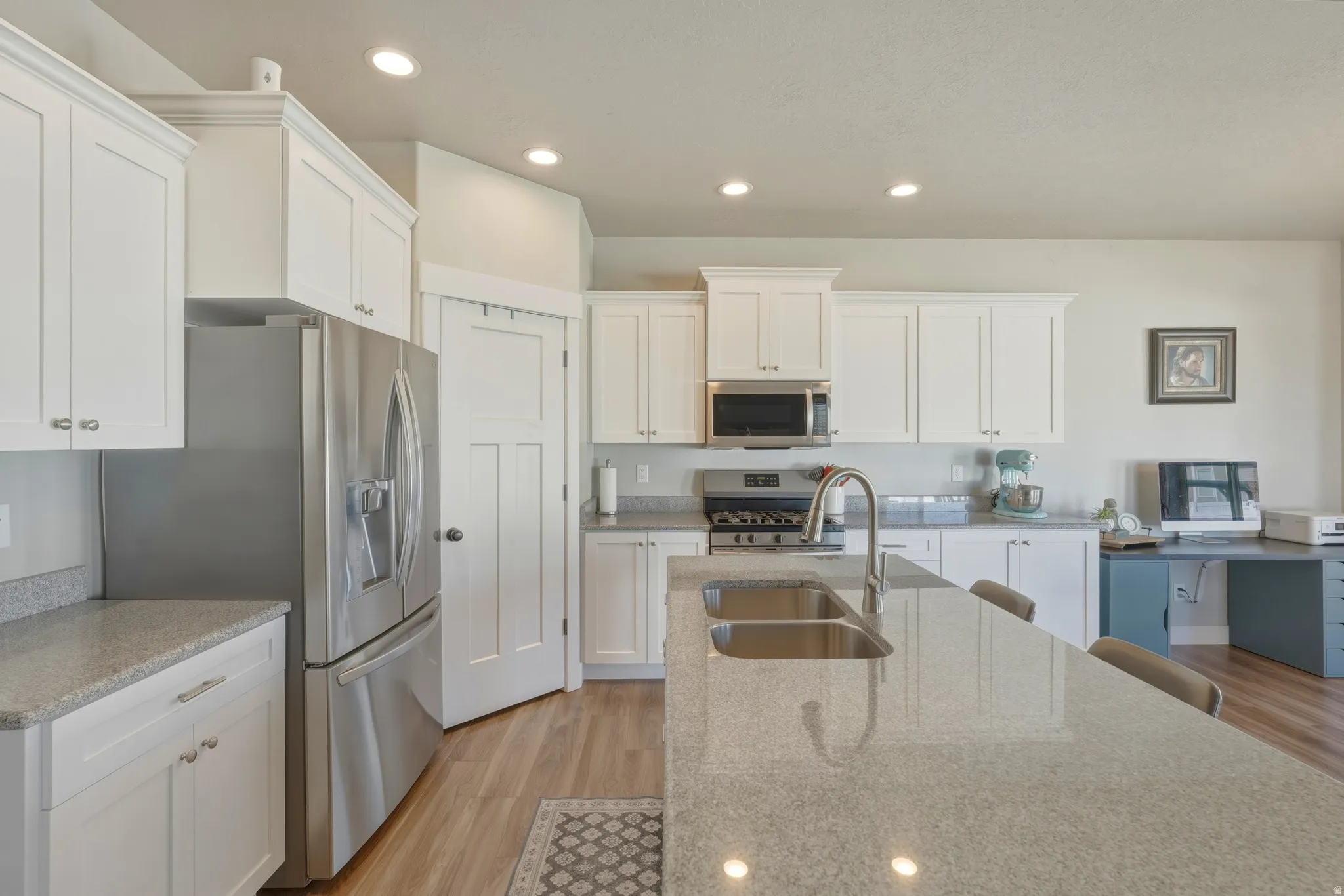 Kitchen with white cabinets, light wood-style flooring, stainless steel appliances, light stone countertops, and recessed lighting