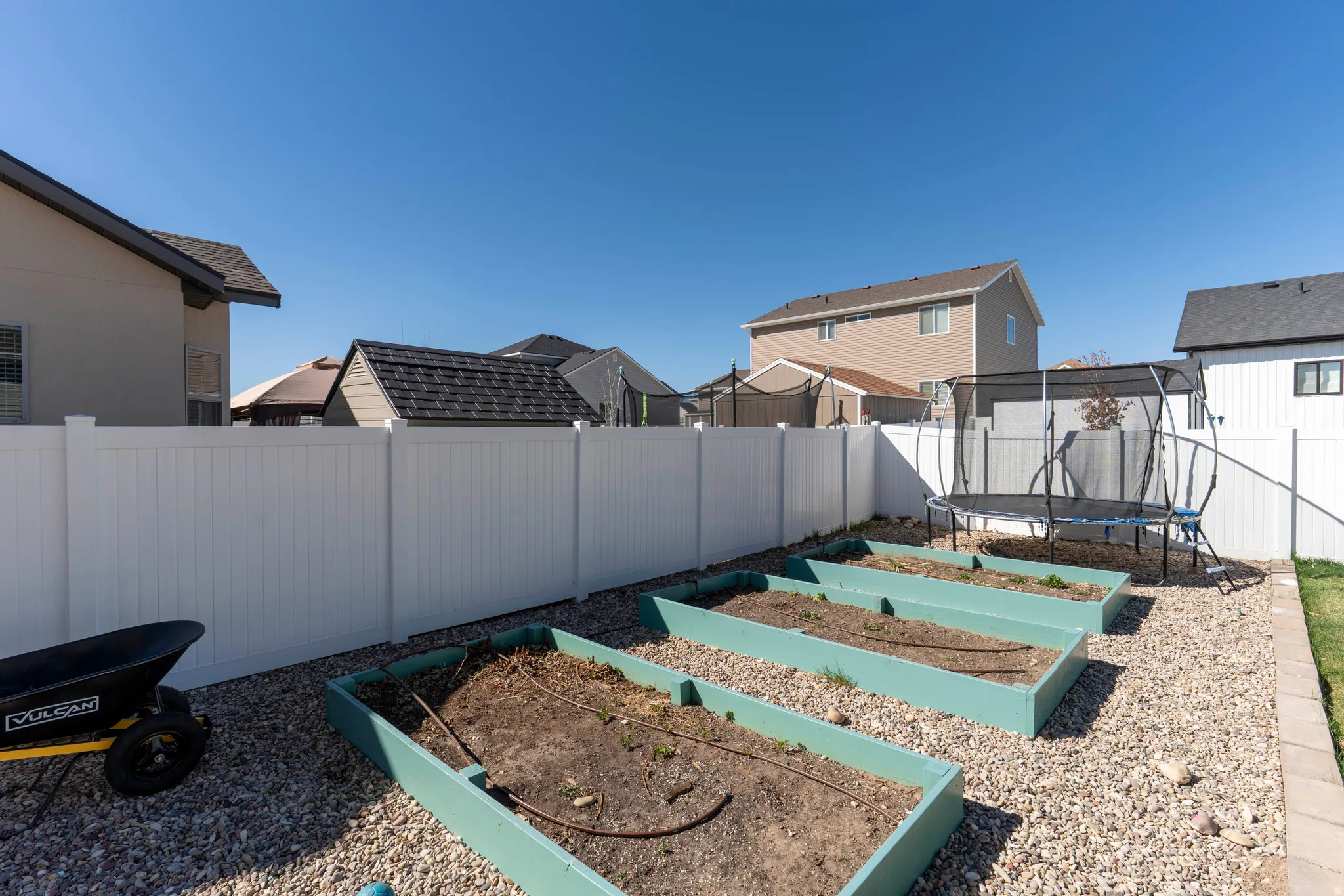 Fenced backyard with a garden, a trampoline, and a residential view