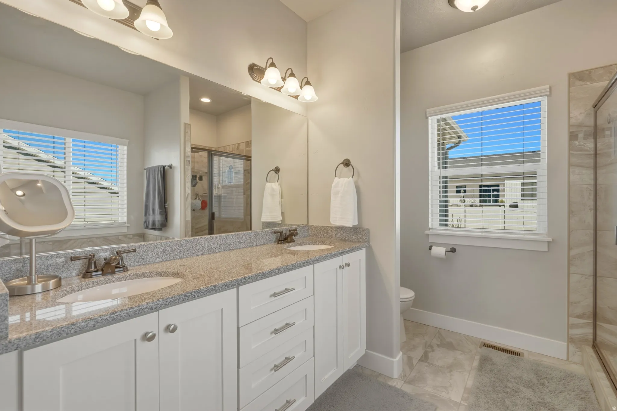 Bathroom with double vanity, a shower stall, and plenty of natural light