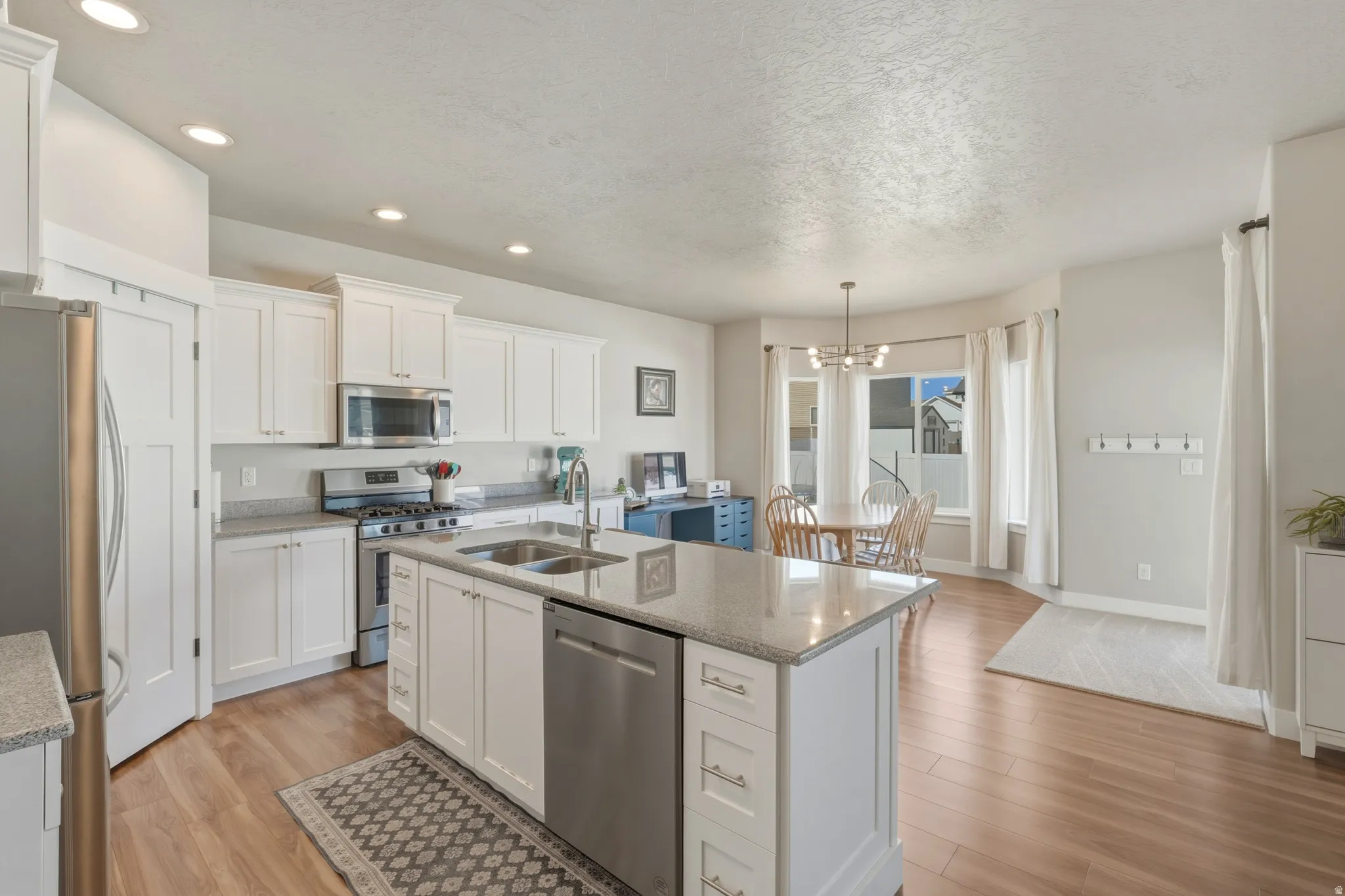 Kitchen featuring light wood-type flooring, white cabinetry, stainless steel appliances, and a textured ceiling