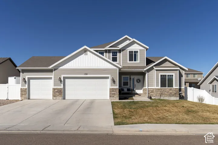 Craftsman-style house with stone siding, an attached garage, driveway, and a gate