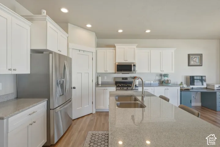 Kitchen with white cabinets, light wood-style flooring, stainless steel appliances, light stone countertops, and recessed lighting
