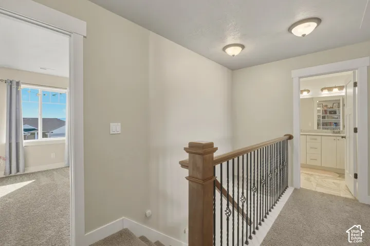 Hallway with light colored carpet and an upstairs landing