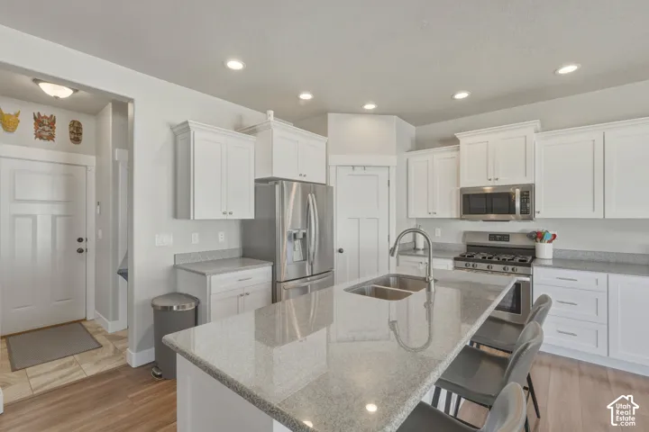 Kitchen with white cabinets, stainless steel appliances, light stone counters, a center island with sink, and recessed lighting