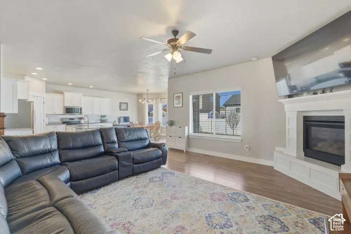 Living room featuring a ceiling fan, dark wood-type flooring, a glass covered fireplace, and a chandelier