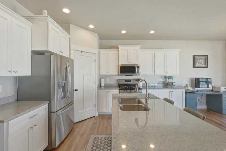 Kitchen with white cabinets, light wood-style flooring, stainless steel appliances, light stone countertops, and recessed lighting