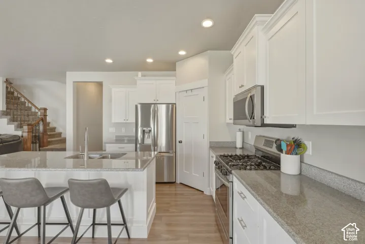 Kitchen with stainless steel appliances, light stone countertops, white cabinets, light wood-style flooring, and recessed lighting