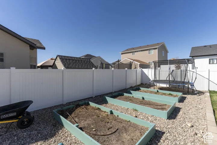 Fenced backyard with a garden, a trampoline, and a residential view