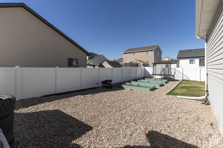Fenced backyard featuring a trampoline, a patio, a residential view, and a garden