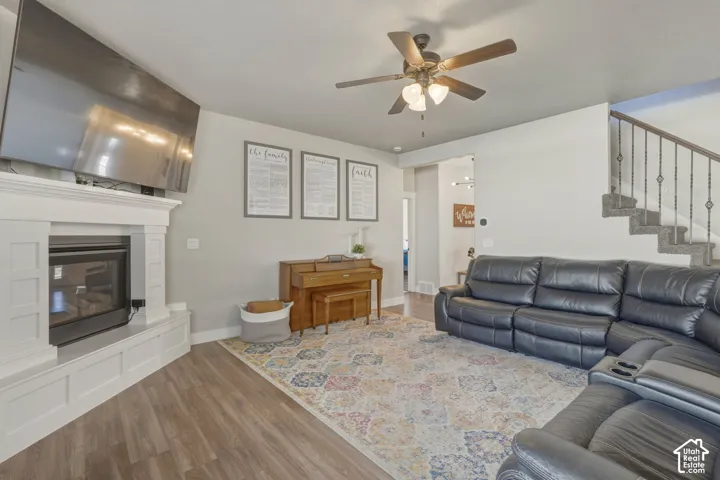 Living room with wood finished floors, a ceiling fan, and a glass covered fireplace