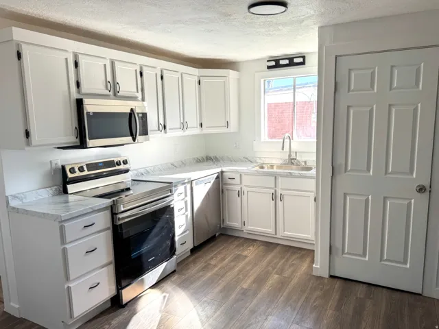 Kitchen featuring stainless steel appliances, light countertops, a textured ceiling, white cabinetry, and dark wood-type flooring