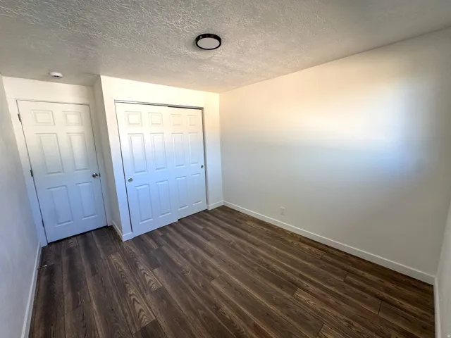 Unfurnished bedroom with a textured ceiling, dark wood-style floors, and a closet