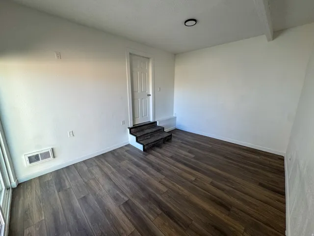 Spare room with dark wood-type flooring and baseboards
