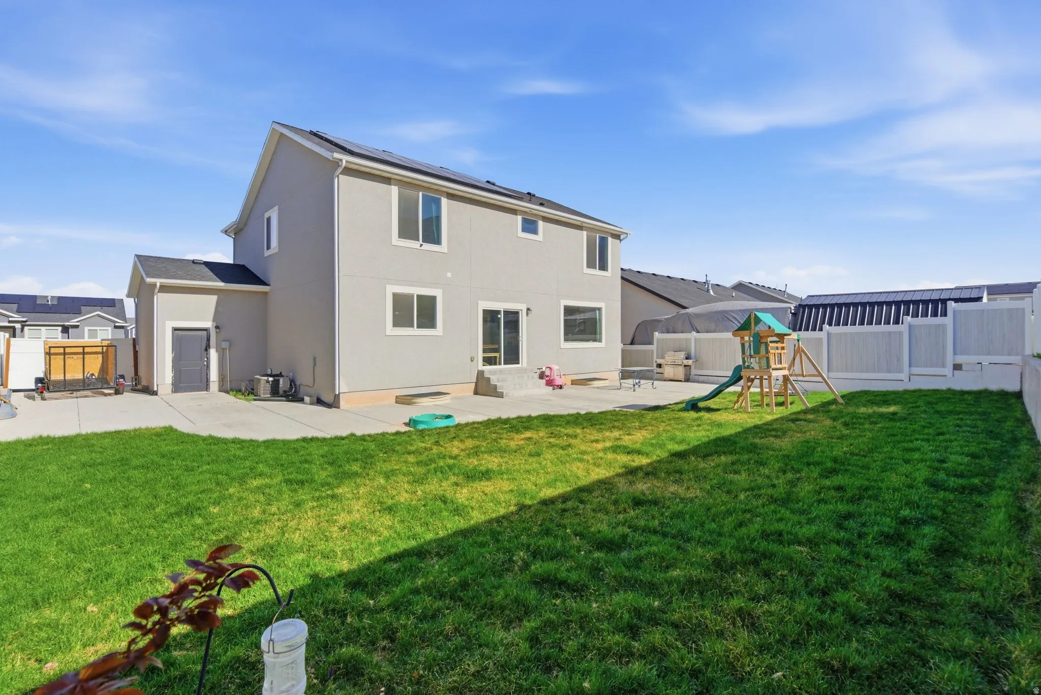 Back of house with solar panels, a patio, a playground, a fenced backyard, and stucco siding
