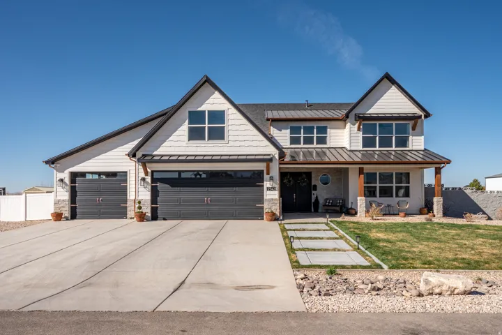 View of front of house featuring a standing seam roof, covered porch, driveway, and stone siding