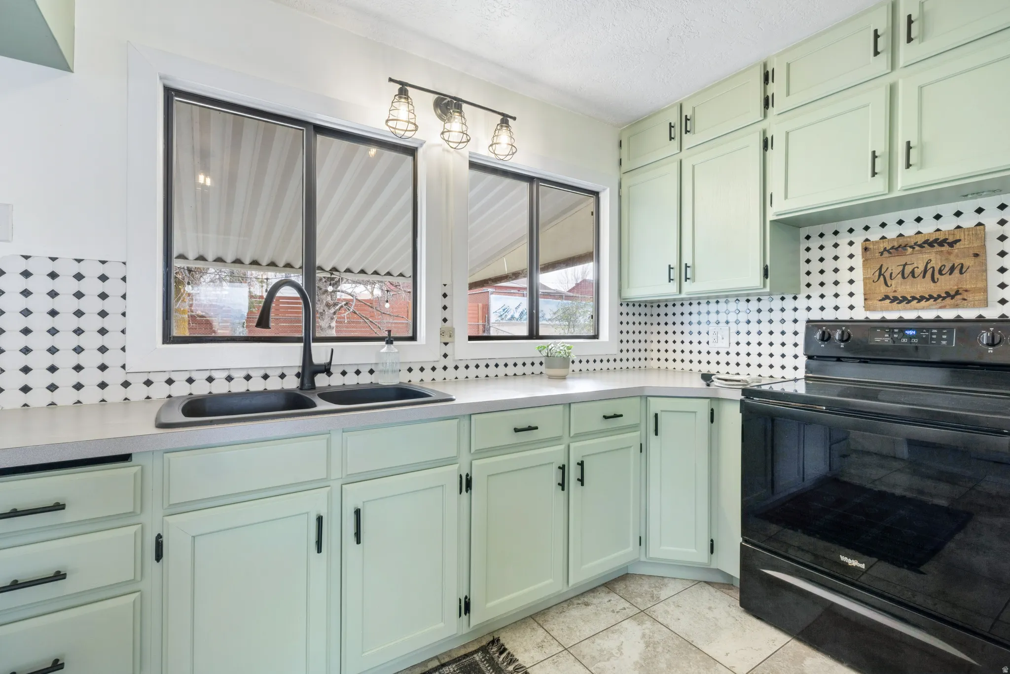 Kitchen featuring green cabinetry, black electric range, decorative backsplash, light countertops, and a textured ceiling