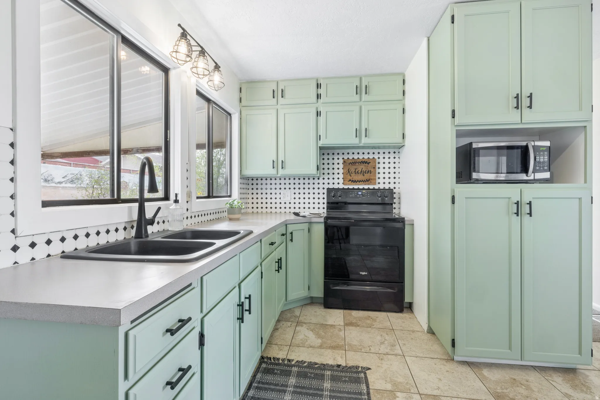 Kitchen featuring green cabinetry, black electric range, tasteful backsplash, stainless steel microwave, and light countertops