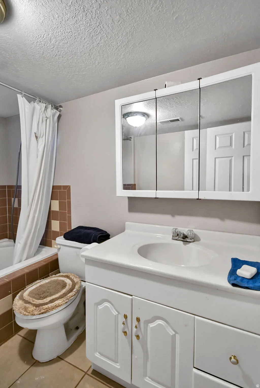 Full bathroom with vanity, a textured ceiling, light tile patterned floors, and tiled shower / bath combo