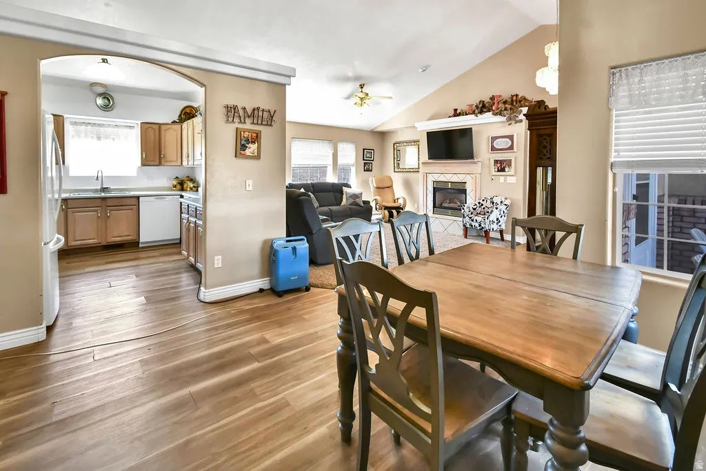 Dining space with light wood-style floors, ceiling fan, vaulted ceiling, a tiled fireplace, and healthy amount of natural light