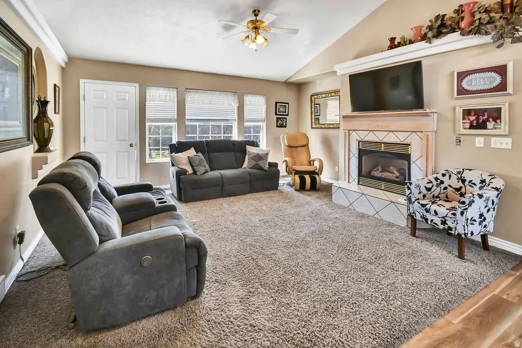 Carpeted living room featuring a ceiling fan, lofted ceiling, and a fireplace