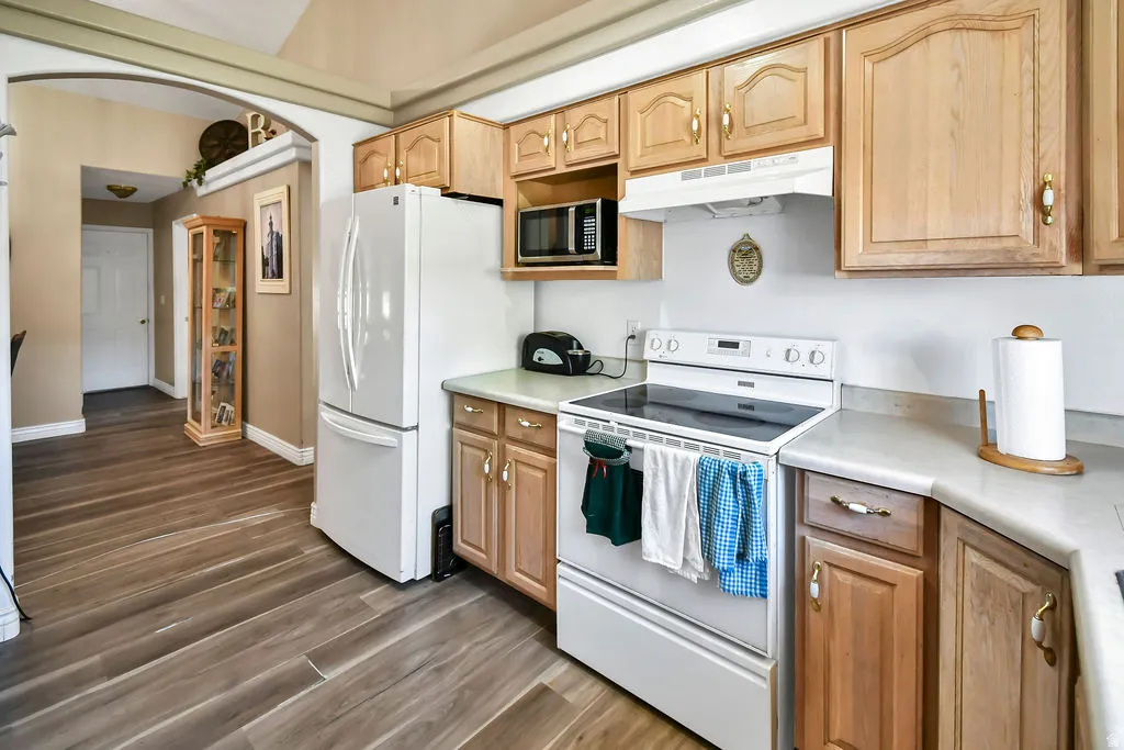Kitchen featuring white appliances, arched walkways, light countertops, dark wood-style floors, and light wood finish cabinets