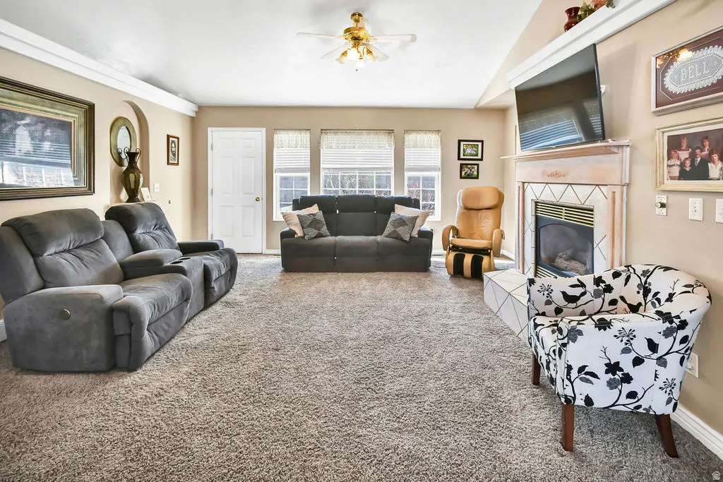 Carpeted living room with a ceiling fan, a tiled fireplace, and lofted ceiling
