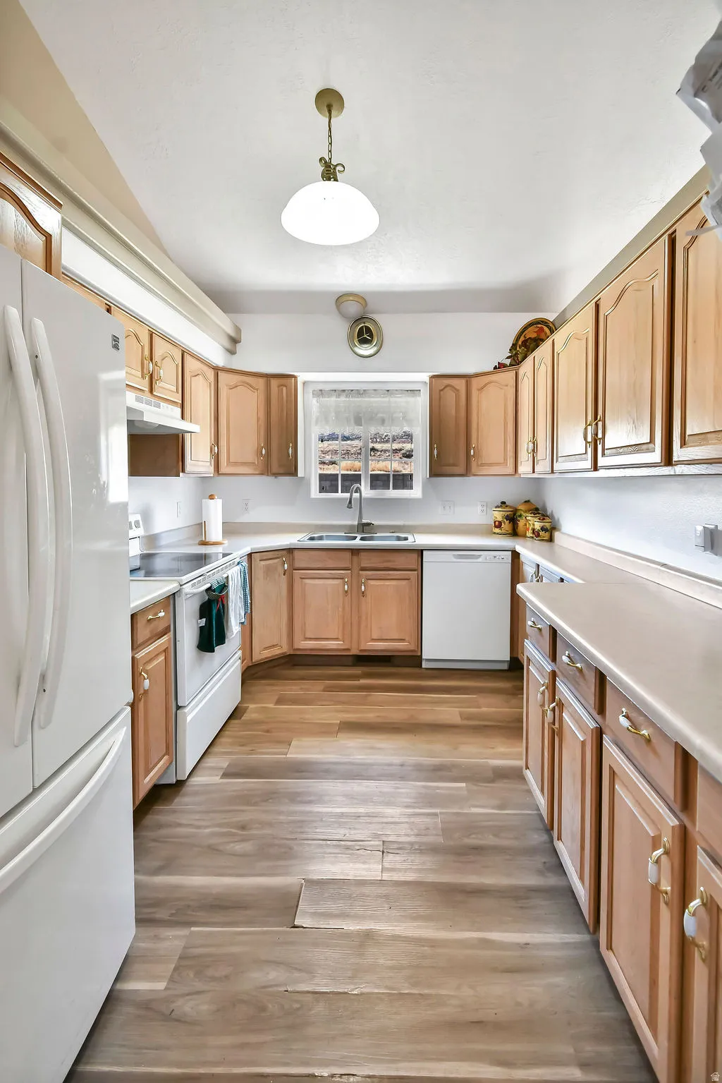 Kitchen featuring white appliances, light countertops, light wood-style floors, and hanging light fixtures