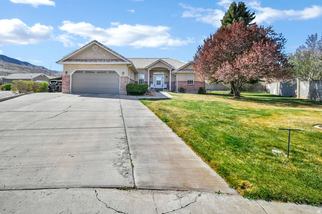 Single story home featuring a garage, driveway, a front lawn, brick siding, and a mountain view