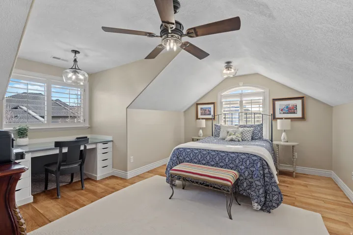 Bedroom with a textured ceiling, light wood-style flooring, multiple windows, ceiling fan, and a desk