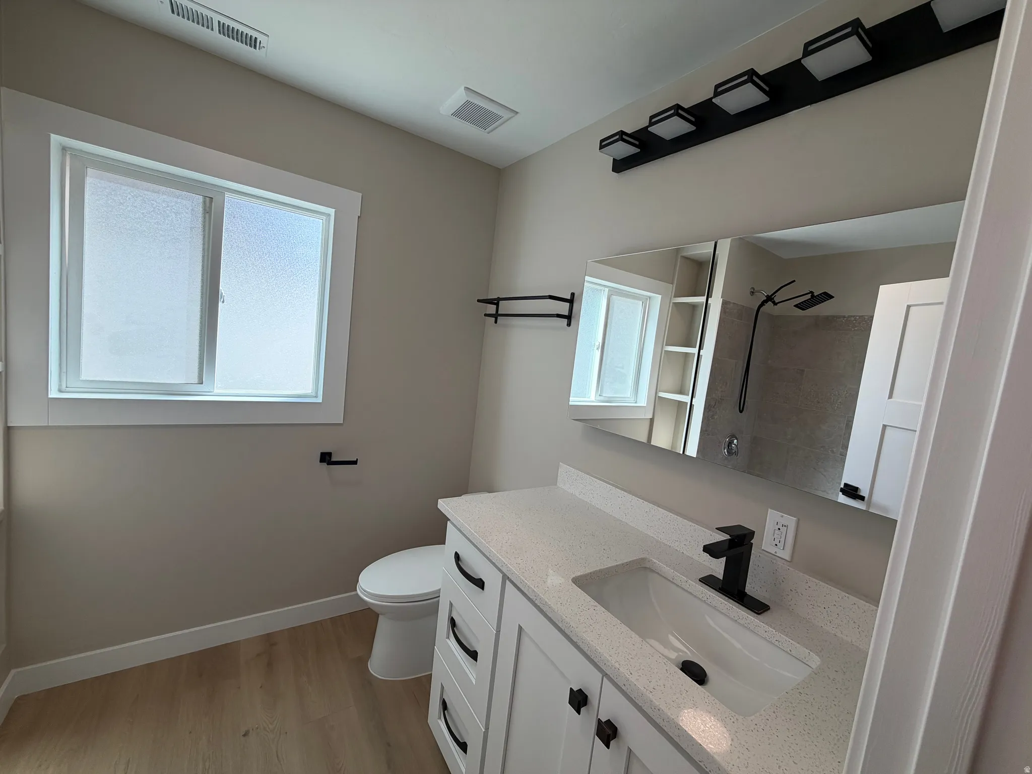 Bathroom with tiled shower, vanity, and light wood-type flooring