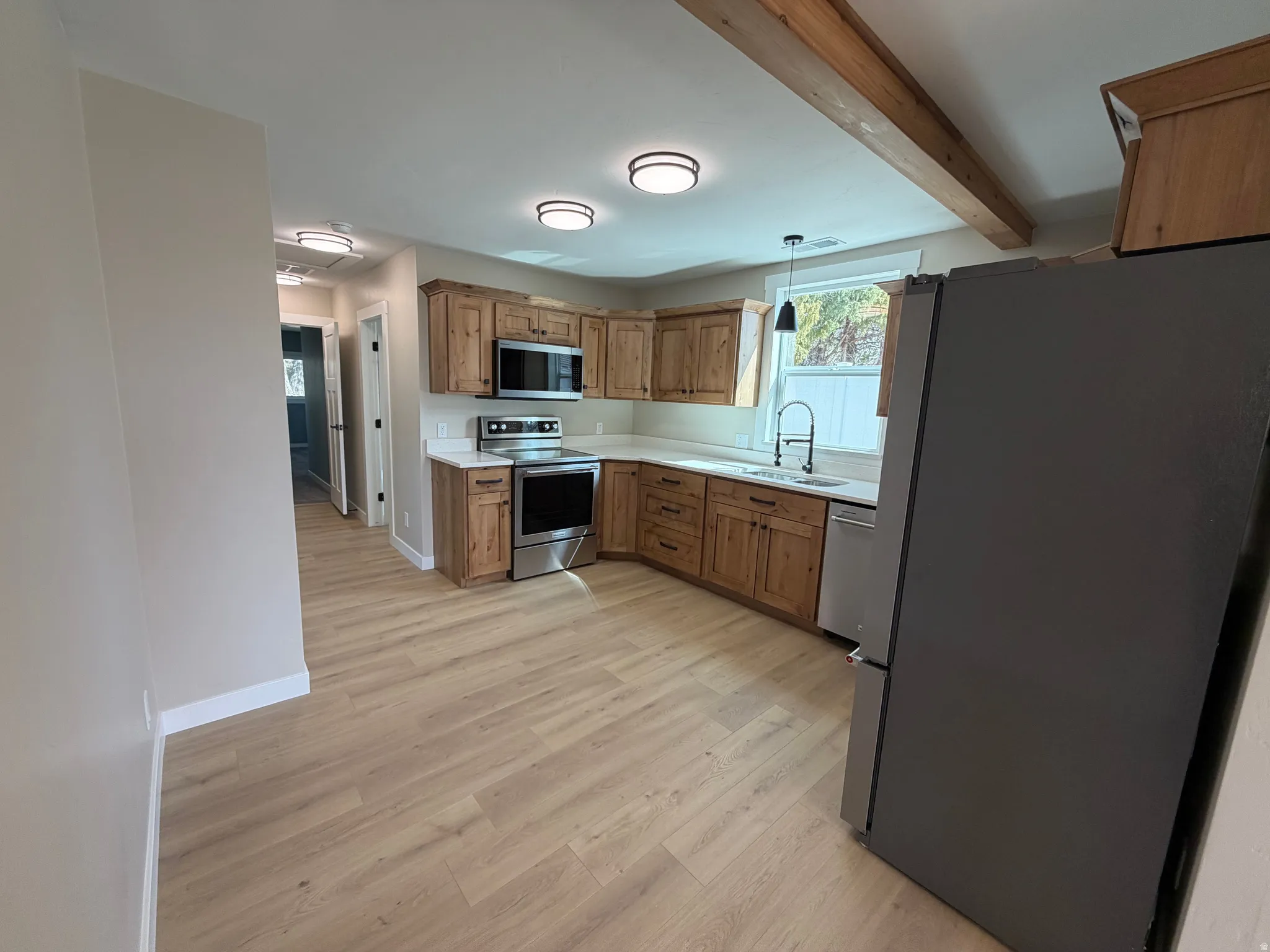 Kitchen featuring stainless steel appliances, wood finish cabinets, light countertops, light wood-type flooring, and hanging light fixtures