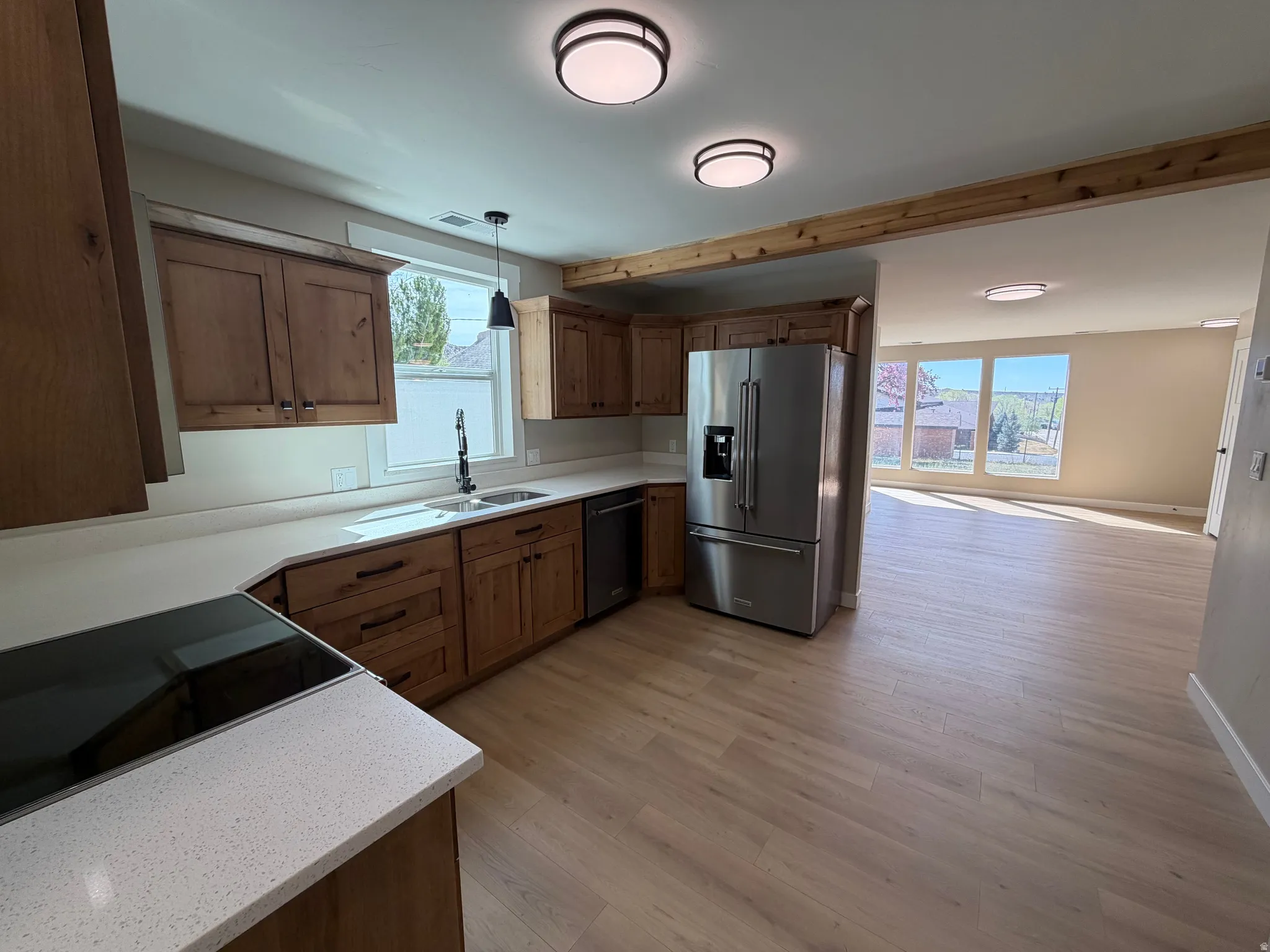 Kitchen featuring black appliances, light wood-type flooring, decorative light fixtures, wood finish cabinetry, and light stone counters