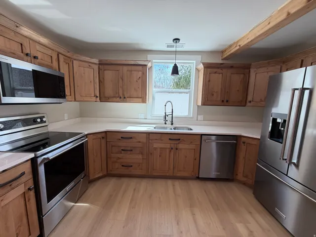 Kitchen with stainless steel appliances, hanging light fixtures, light wood-style floors, and wood finish cabinets