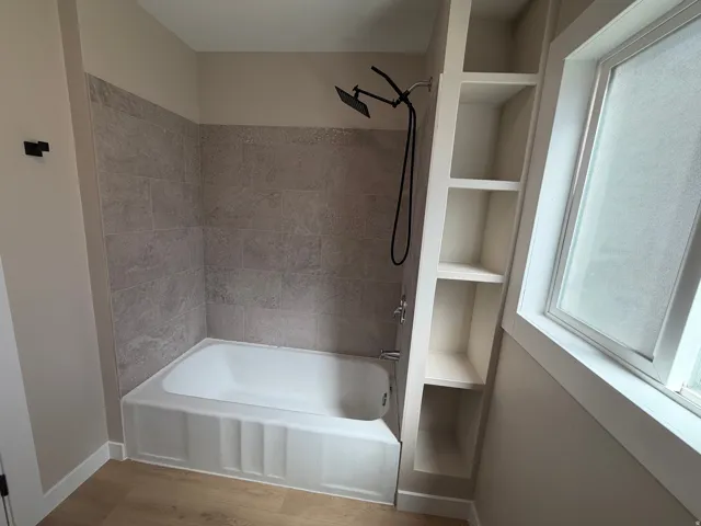 Bathroom with washtub / shower combination and light wood-style flooring