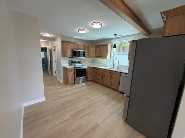Kitchen featuring stainless steel appliances, wood finish cabinets, light countertops, light wood-type flooring, and hanging light fixtures