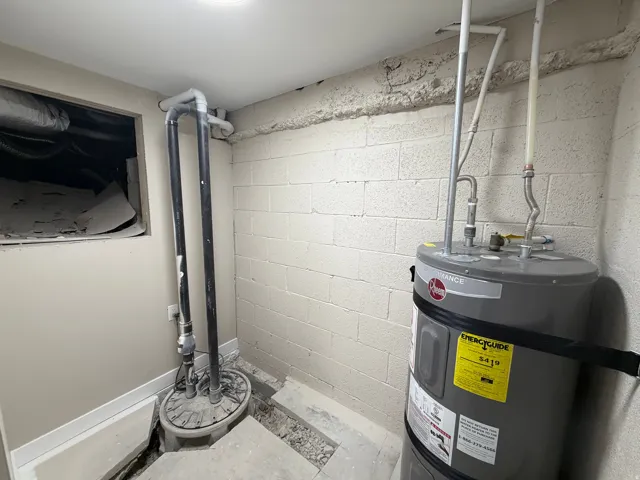 Utility room featuring strapped water heater and drainage system