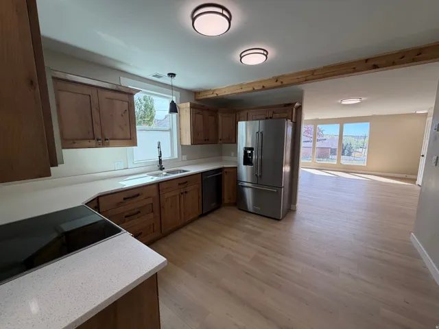 Kitchen featuring black appliances, light wood-type flooring, decorative light fixtures, wood finish cabinetry, and light stone counters