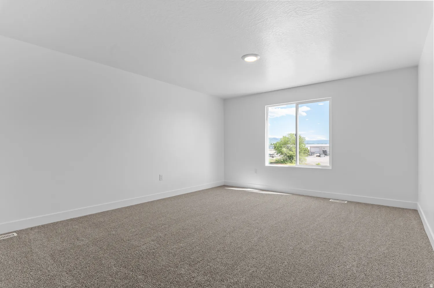 Spacious room featuring neutral carpeting, white walls, a large window, and recessed ceiling lighting