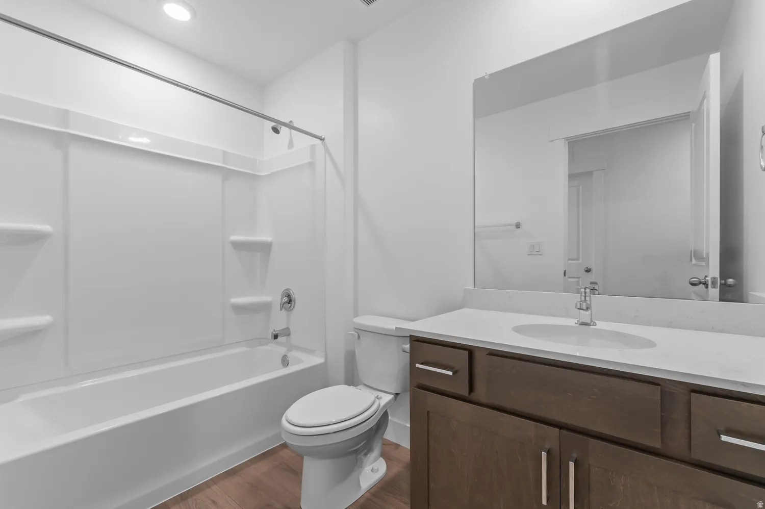 White bathtub and shower combination with chrome fixtures, dark wood-finish vanity with a light-colored countertop, and a large wall-mounted mirror