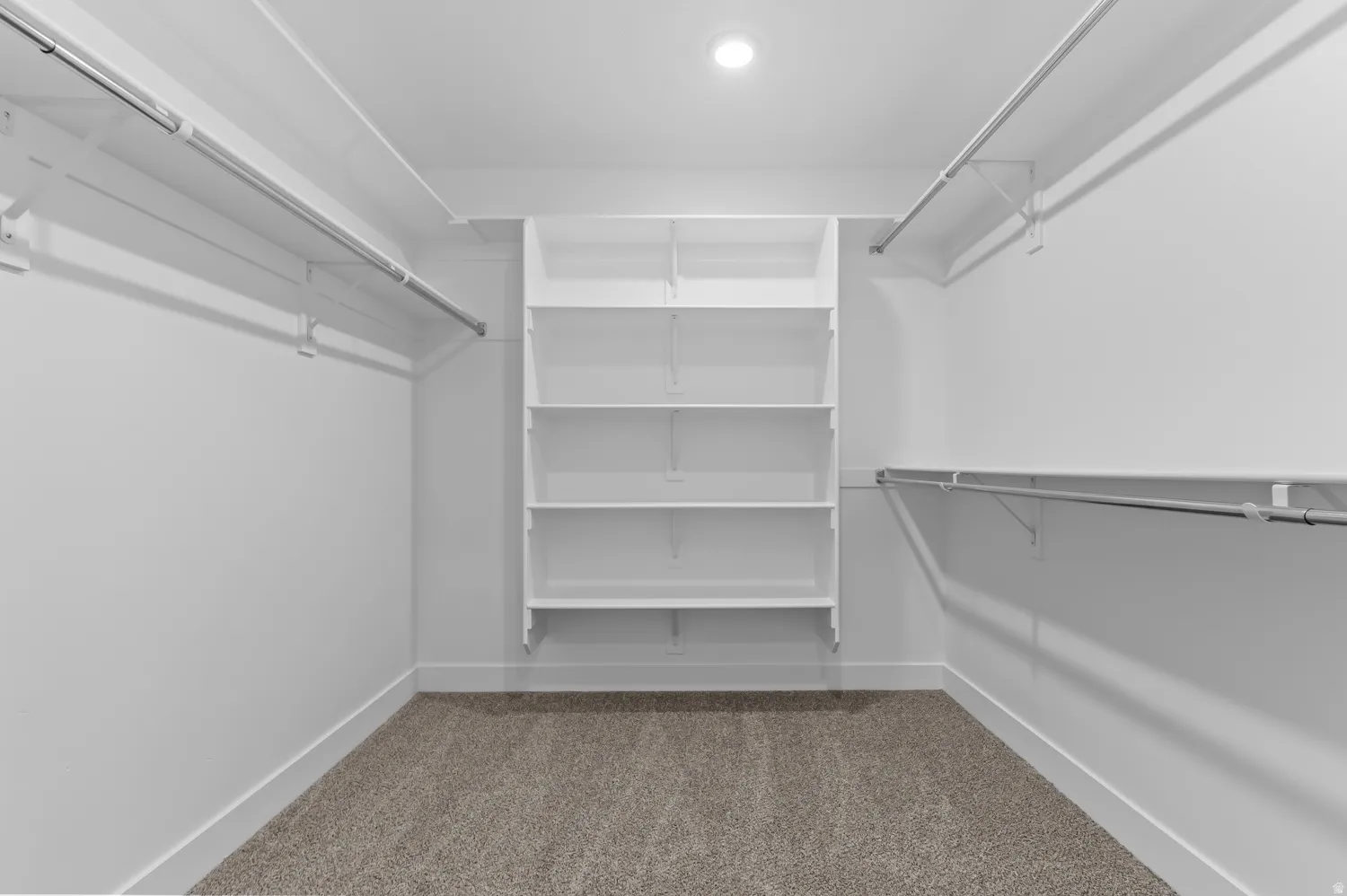 Recessed lighting illuminates the walk-in closet, featuring a built-in shelving unit, dual clothing rods, and carpet flooring
