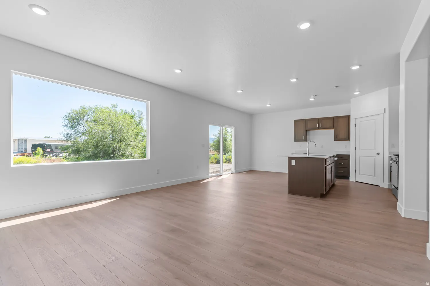 Expansive open-concept living area featuring wood-finish flooring, a large horizontal window, and recessed lighting