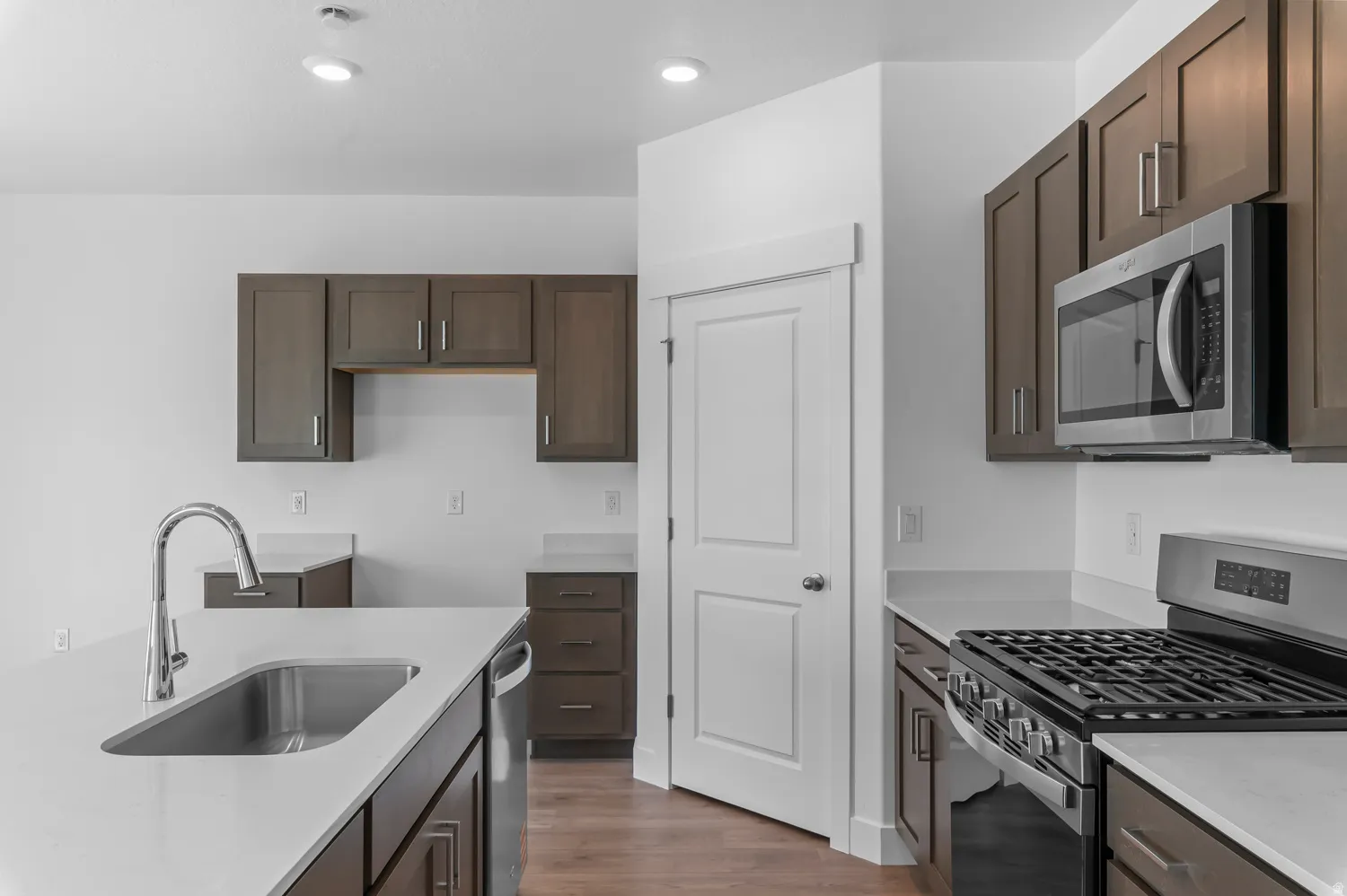 Contemporary kitchen featuring dark wood cabinetry, light-toned countertops, and stainless steel appliances including a range and microwave