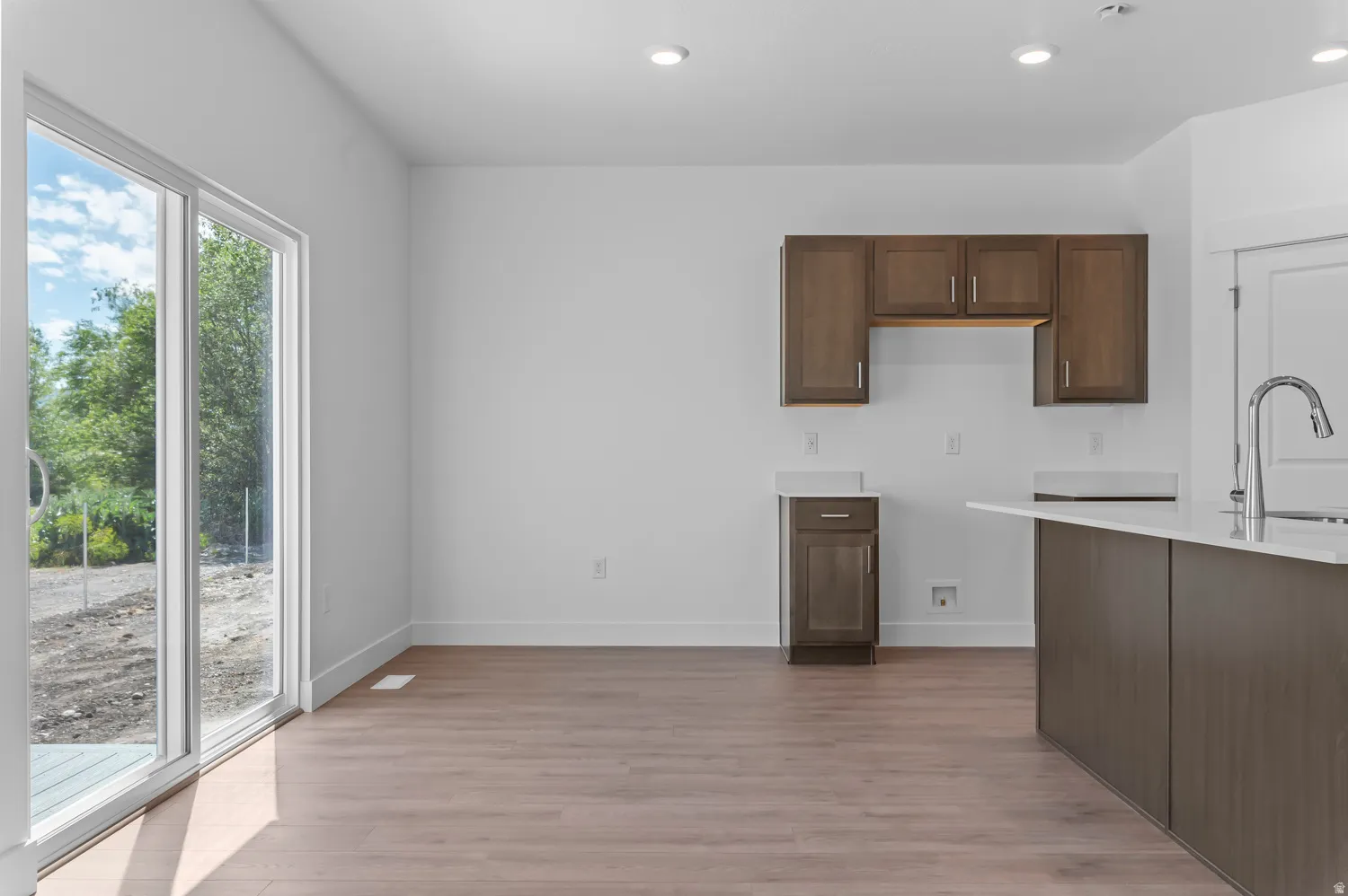 Sliding glass door, wood-finish flooring, recessed lighting, dark wood-finish cabinetry, white countertops