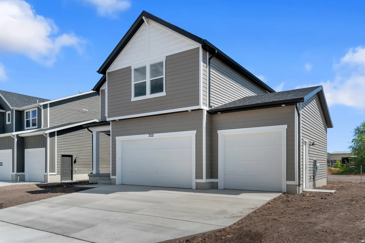 Gray siding exterior with white trim, a gabled roof, two white garage doors, and an extended concrete driveway