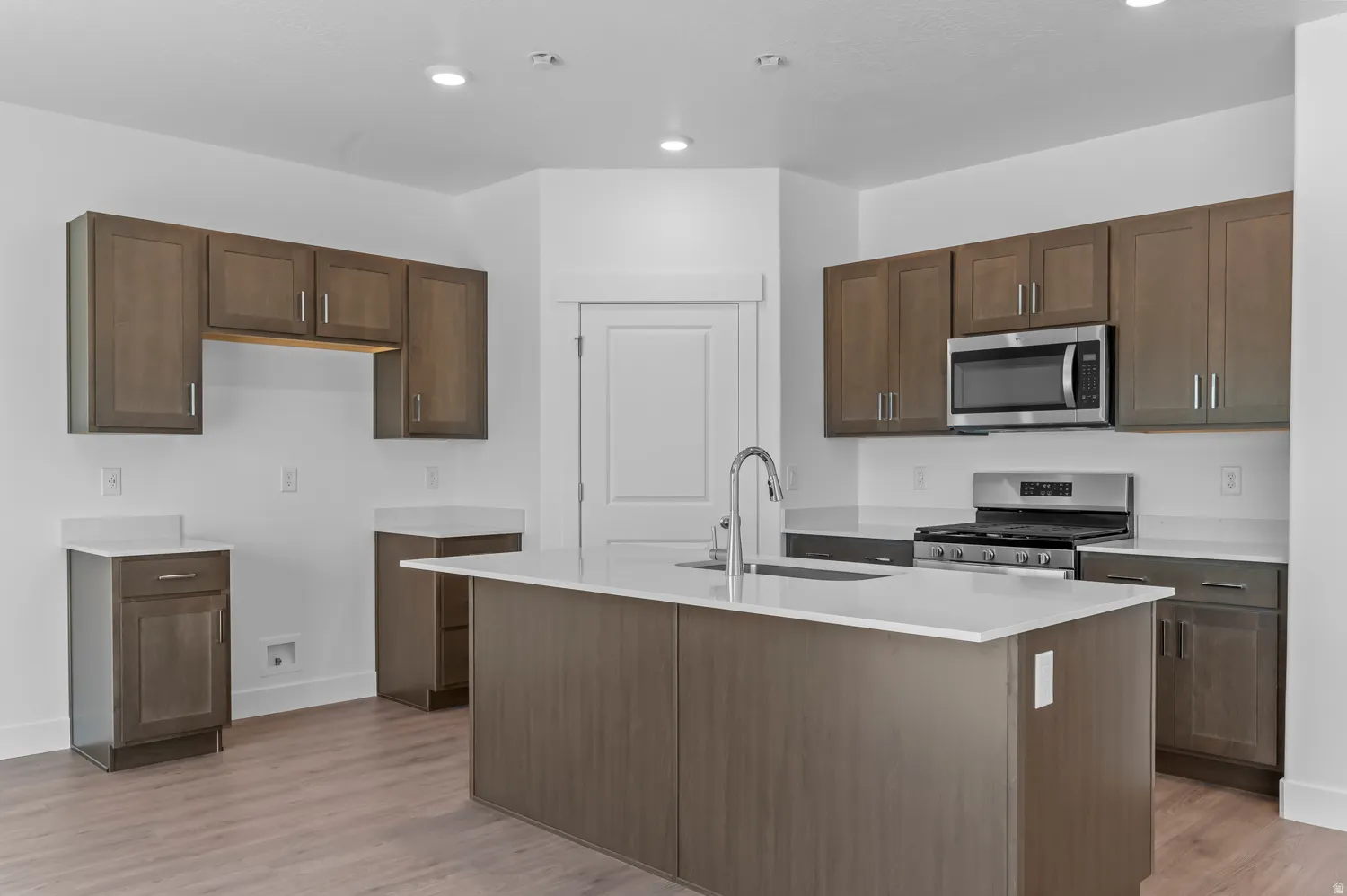 Kitchen featuring a central island with a sink, stainless steel appliances, wood-finish flooring, and recessed lighting