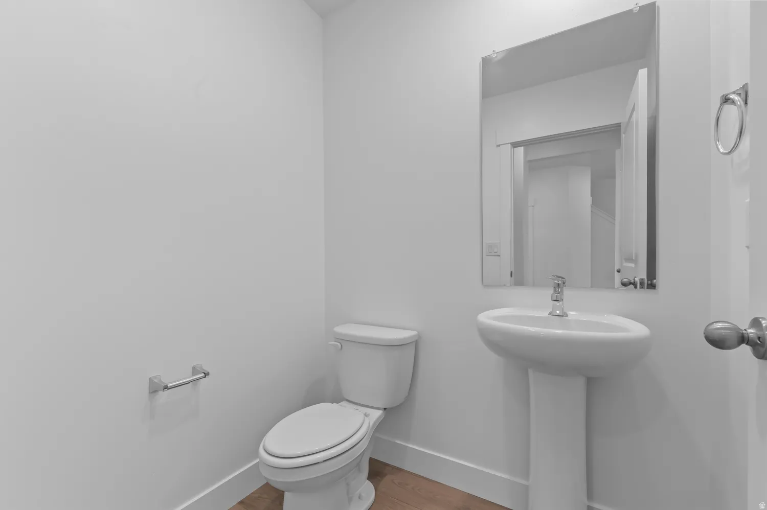 White pedestal sink, modern chrome faucet, wall-mounted mirror, and wood-finish flooring