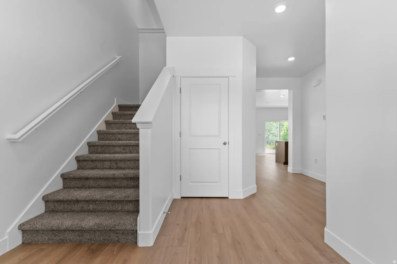 Carpeted staircase with white handrail, wood-finish flooring, recessed lighting, and white interior doors